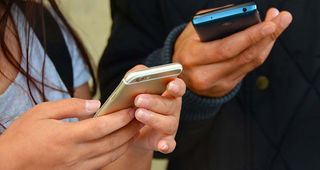 two people holding different types of devices to receive emails, text messages, or phone calls.